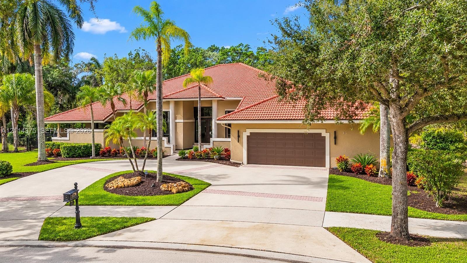 Stucco exterior featuring a terracotta tile roof, an oversized multi-car garage, and a paver-accented concrete driveway situated within a landscaped l