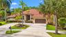 Stucco exterior featuring a terracotta tile roof, an oversized multi-car garage, and a paver-accented concrete driveway situated within a landscaped l