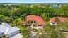 Aerial perspective featuring a multi-hipped clay tile roof, expansive manicured lawn, established palm landscaping, and concrete driveway