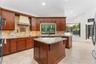 Kitchen featuring stained wood cabinetry, stone countertops, a center island with corbel detailing, a tiled backsplash, and recessed lighting