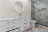 White cabinetry vanity with rectangular vessel sink, frameless glass shower enclosure with stone-tile surround, built-in shower niche, and round wall-