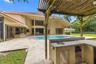 Outdoor kitchen featuring stone-finish counters, integrated sink, and stainless-steel cabinetry under a wooden pergola, situated on a stone-paver pati