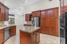 Kitchen featuring full-height stained wood cabinetry, stone countertops, central island, double wall oven, and tile flooring under a vaulted ceiling