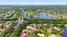 Aerial perspective of a residential community featuring winding waterways, dense clusters of mature trees, paved road infrastructure, and varying roof