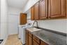Laundry room featuring wood-finish cabinetry, stone-texture countertop, drop-in basin sink, matte black gooseneck faucet, and tile flooring