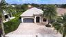 Single-story residence featuring a tile roof, paved driveway, two-car garage, and established landscaping