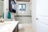 Bathroom featuring a dark-finish vanity with a stone-top integrated sink, a tiled shower-tub combination with sliding glass doors and decorative mosai