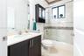 Dark-finish cabinetry vanity with stone-surfaced countertop, integrated sink, mirrored medicine cabinet, and shower-tub combination featuring tiled de