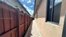 Stucco exterior wall featuring dark-framed windows and a stone-paver side path bordered by a wood privacy fence