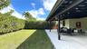 Covered patio featuring paver flooring, overhead support beams, recessed lighting, and a manicured lawn bordered by a tall privacy hedge