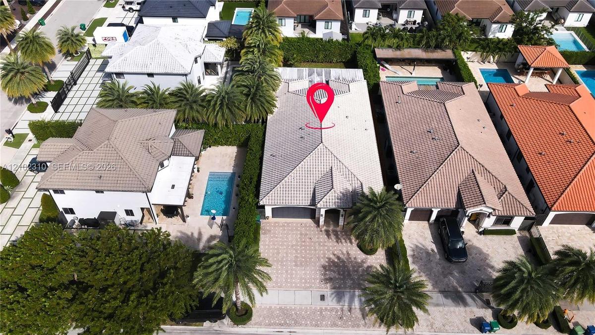 Aerial perspective of property featuring a tile roof, paved driveway, two-car garage, and established perimeter landscaping