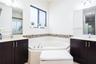 Dual dark wood cabinetry with neutral countertops, recessed corner soaking tub, tile backsplash, and oversized vanity mirrors