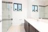 Walk-in shower with a glass enclosure, dark cabinetry with a solid-surface countertop, rectangular undermount sink, and mosaic tile wall accents