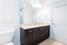 Dark-finish wood cabinetry, integrated stone-composite countertop with an oval under-mount sink, chrome hardware, full-width vanity mirror, and three-