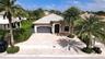 Single-story exterior featuring a concrete tile roof, paver driveway, two-car garage, and mature palm trees