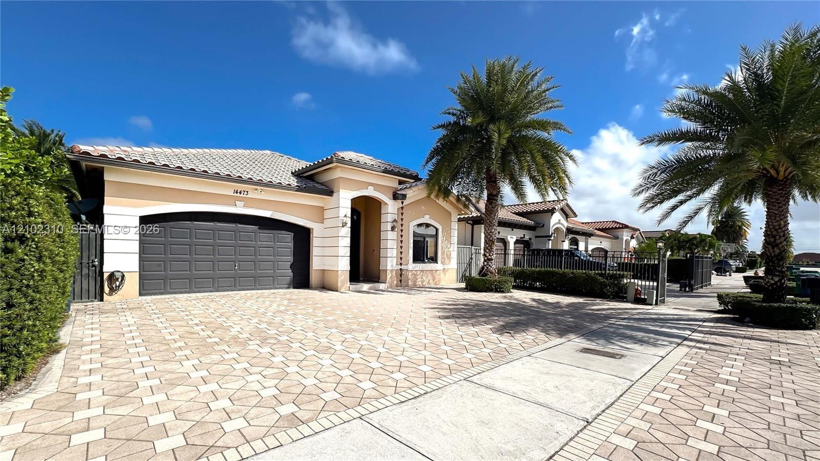 Stucco exterior residence featuring a tiled roof, arched entryway, multi-car garage, and decorative paved driveway