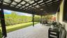 Covered patio featuring a timber-frame pergola, paver flooring, and a manicured lawn enclosed by mature privacy hedges
