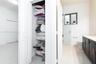 Dark wood-finish cabinetry, light-toned countertop, wire shelving unit, white tile flooring, and a glass-enclosed shower