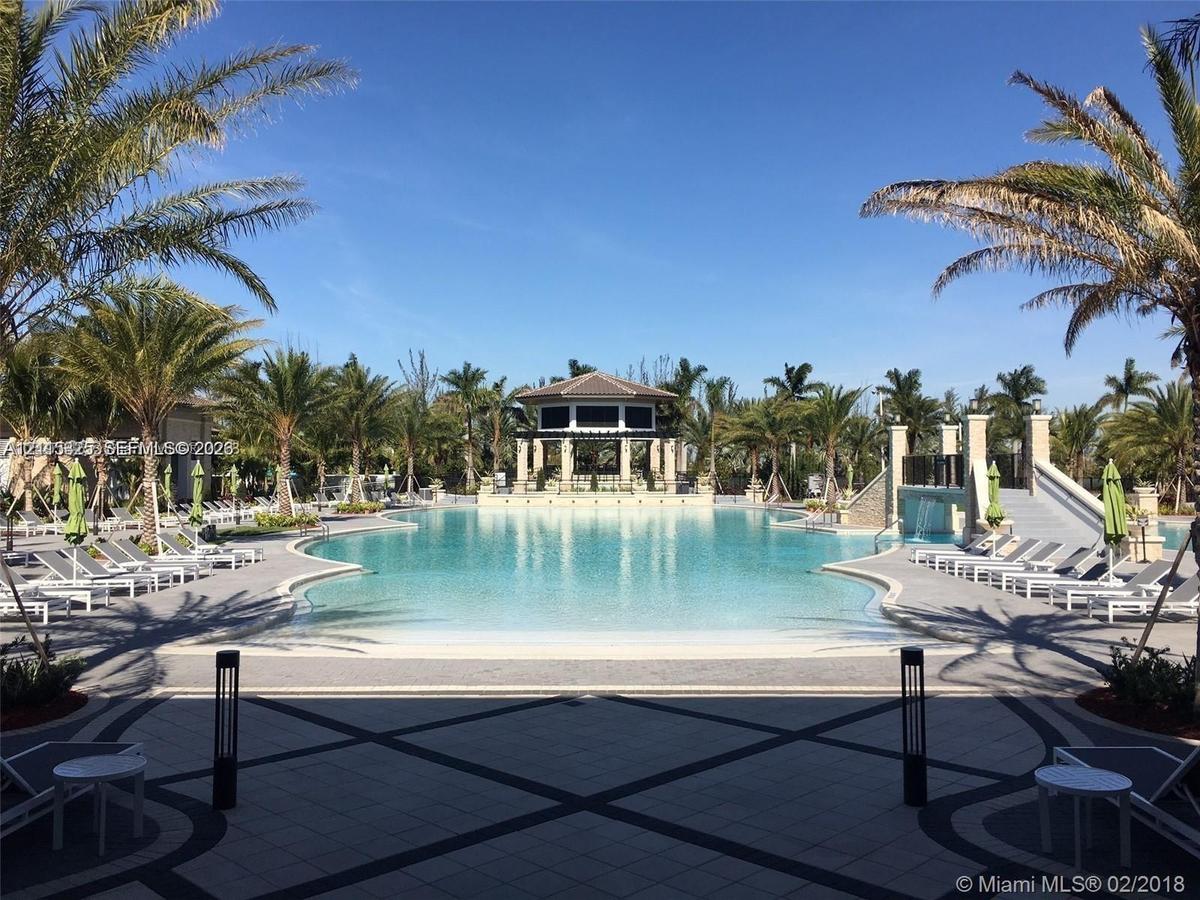Swimming pool featuring a beach-style entry, a central gazebo, stone-tiled decking, a decorative water feature, and integrated landscape lighting