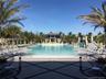 Swimming pool featuring a beach-style entry, a central gazebo, stone-tiled decking, a decorative water feature, and integrated landscape lighting
