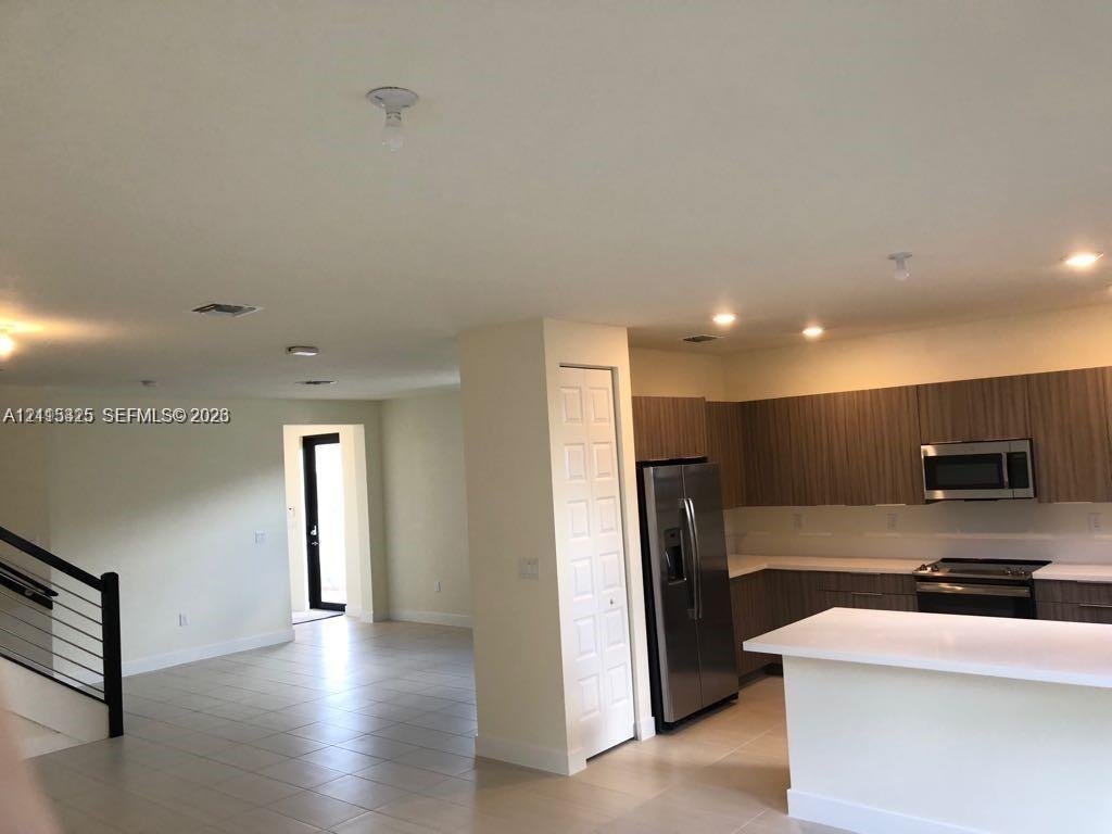 Kitchen featuring flat-panel wood-finish cabinetry, quartz countertops, a kitchen island, and stainless steel appliances, including a built-in microwa
