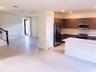 Kitchen featuring horizontal-grain cabinetry, quartz countertops, a stainless steel refrigerator, and a built-in microwave, accented by a staircase wi