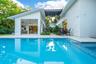In-ground swimming pool with tiled border, expansive stone-paved patio, covered outdoor kitchen with stainless steel appliances, and minimalist white 
