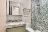Modern vanity with a natural stone countertop and brass-finish faucet, featuring a mirrored medicine cabinet, a wall-mounted brass towel rack, and a g