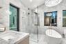 Stone tile wall and floor surfaces, glass-enclosed walk-in shower with gold-tone fixtures, freestanding soaking tub with floor-mounted faucet, and cus