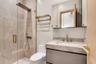 Bathroom featuring a glass-enclosed shower with a rainfall showerhead, stone-finish vanity countertop with an integrated basin, brushed gold-tone fixt
