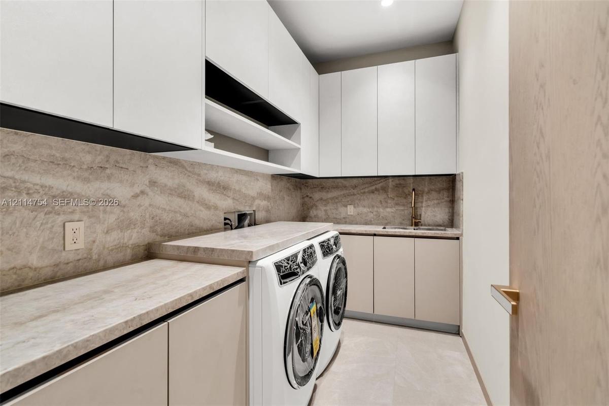 Laundry room featuring floor-to-ceiling cabinetry, stone-patterned backsplash, expansive stone-finish countertop, integrated sink with metallic faucet