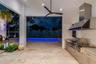 Outdoor kitchen featuring stainless steel cabinetry, integrated grill, and a professional-grade range hood, complemented by stone flooring and an in-g
