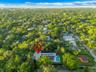 Aerial perspective of a property featuring a private swimming pool, flat roofline, paved patio, and dense mature perimeter landscaping