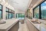 Modern kitchen featuring a waterfall-edge island, stone-surfaced countertops, custom wood-finish cabinetry, floor-to-ceiling black-framed windows, and