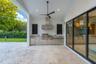 Covered patio featuring stone tile flooring, stainless steel outdoor kitchen with built-in grill, stone countertop, ceiling fan, and expansive sliding