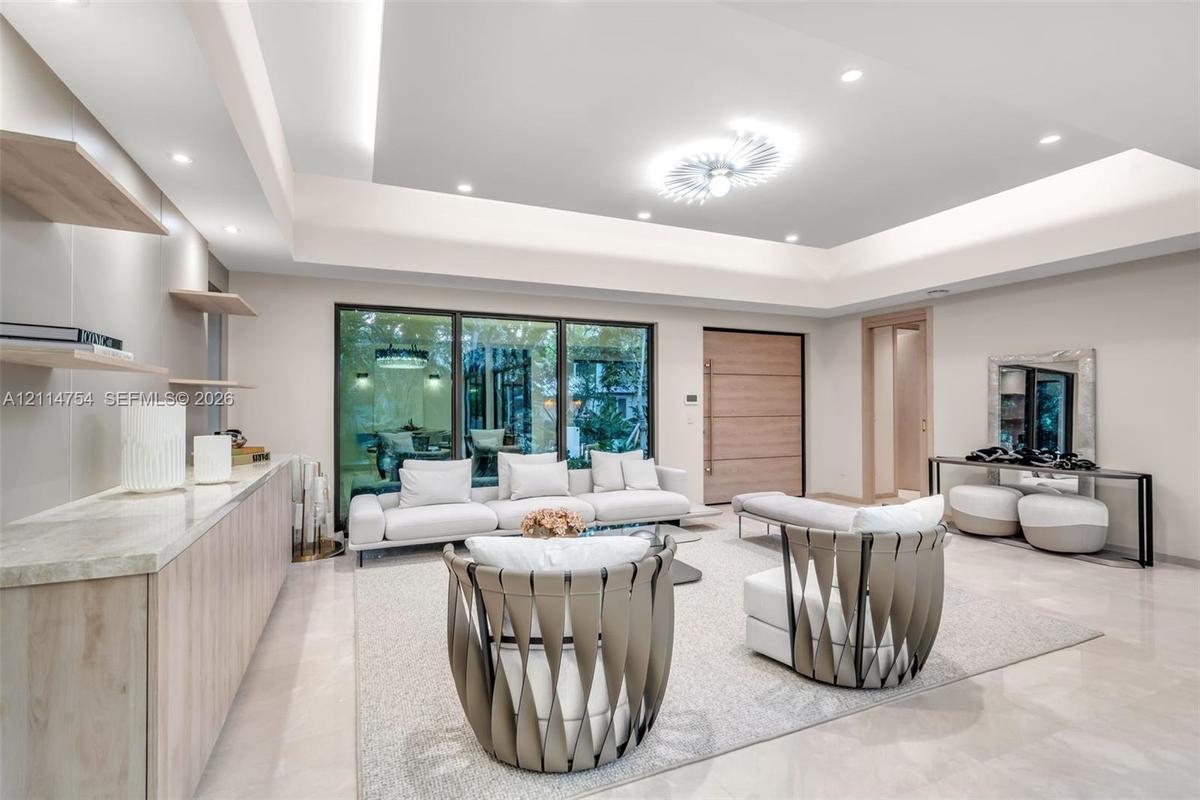 Tray ceiling with recessed lighting, integrated wood-finish cabinetry with stone countertop, floating wall shelves, large-format tile flooring, and fl