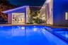 Modern swimming pool featuring stone deck surround, covered outdoor kitchen with stainless steel appliances, and a wood-slat overhead pergola