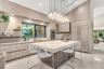 Kitchen featuring a large central island with a thick-profile stone countertop, flat-panel cabinetry, integrated refrigerator, multi-tiered pendant li