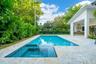 Backyard featuring a rectangular swimming pool with integrated spa, stone-finish decking, covered patio, and built-in outdoor kitchen with stainless s
