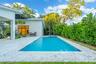 Rectangular swimming pool surrounded by stone-finish decking, covered patio space, and mature perimeter landscaping