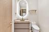 Oval LED-backlit mirror, vanity with integrated stone-finish countertop and brass-tone faucet, soft-close drawers, wall-mounted metallic shelving, and