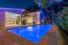 In-ground swimming pool with stone deck, covered patio, integrated pergola, and sliding glass wall systems