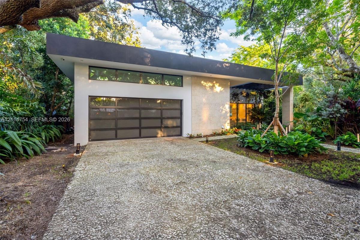Contemporary exterior featuring a flat roofline, stone facade, multi-panel garage door with frosted glass, transom windows, and a paved stone driveway