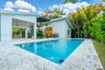 Swimming pool with stone-tiled decking, covered patio with integrated ceiling fan, and exterior wall cladding