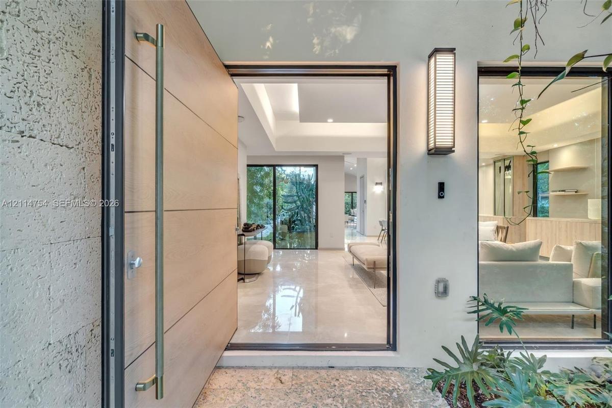 Pivot entry door featuring a light-toned wood finish and a long cylindrical metal handle, textured stone exterior wall, vertical wall-mounted exterior