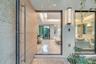 Pivot entry door featuring a light-toned wood finish and a long cylindrical metal handle, textured stone exterior wall, vertical wall-mounted exterior
