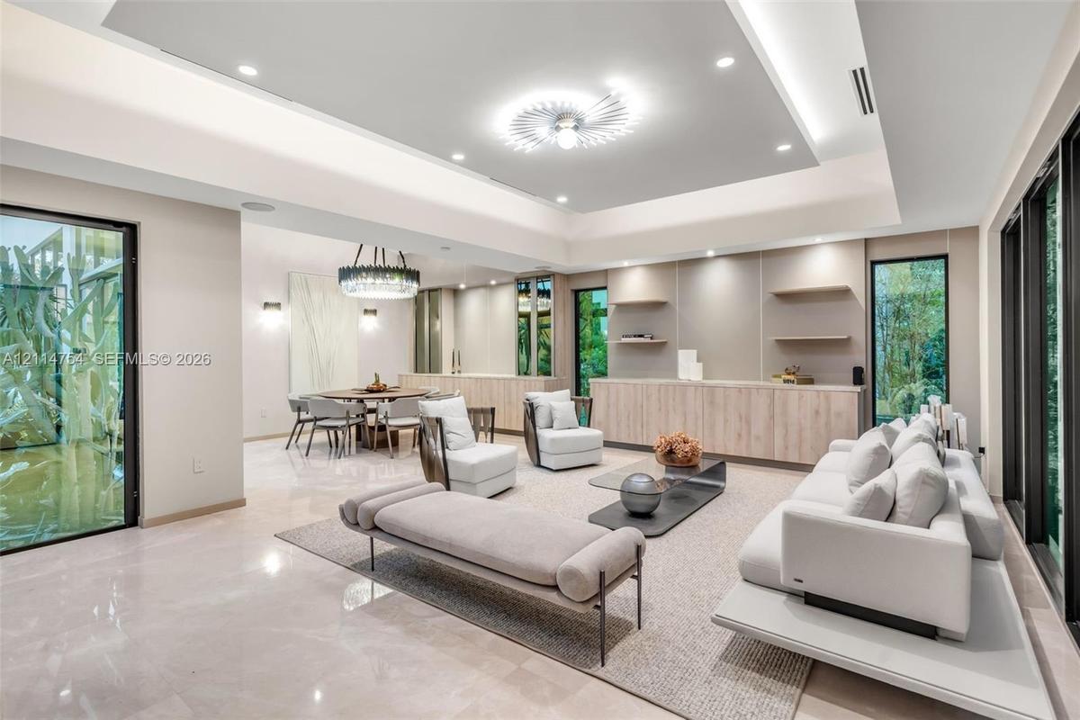 Expansive open-concept living area featuring a recessed tray ceiling with integrated cove lighting, polished stone flooring, custom built-in cabinetry