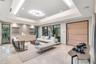 Tray ceiling with cove lighting, expansive floor-to-ceiling glass paneling, polished stone flooring, custom built-in cabinetry with floating shelving,