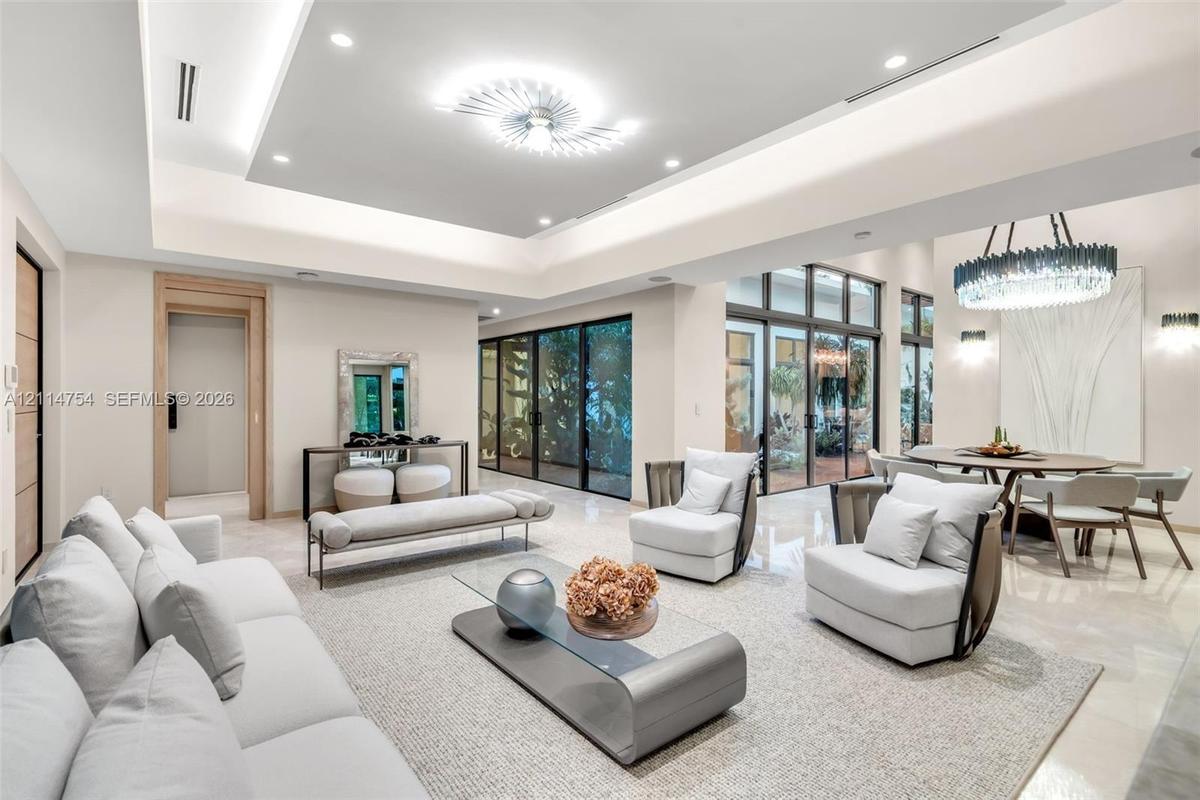 Expansive living area featuring a tray ceiling with recessed lighting, large-format polished flooring, floor-to-ceiling glass wall panels with dark fr
