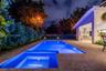Outdoor area featuring a tiled pool and spa with built-in lighting, expansive stone-finish patio, and mature perimeter landscaping
